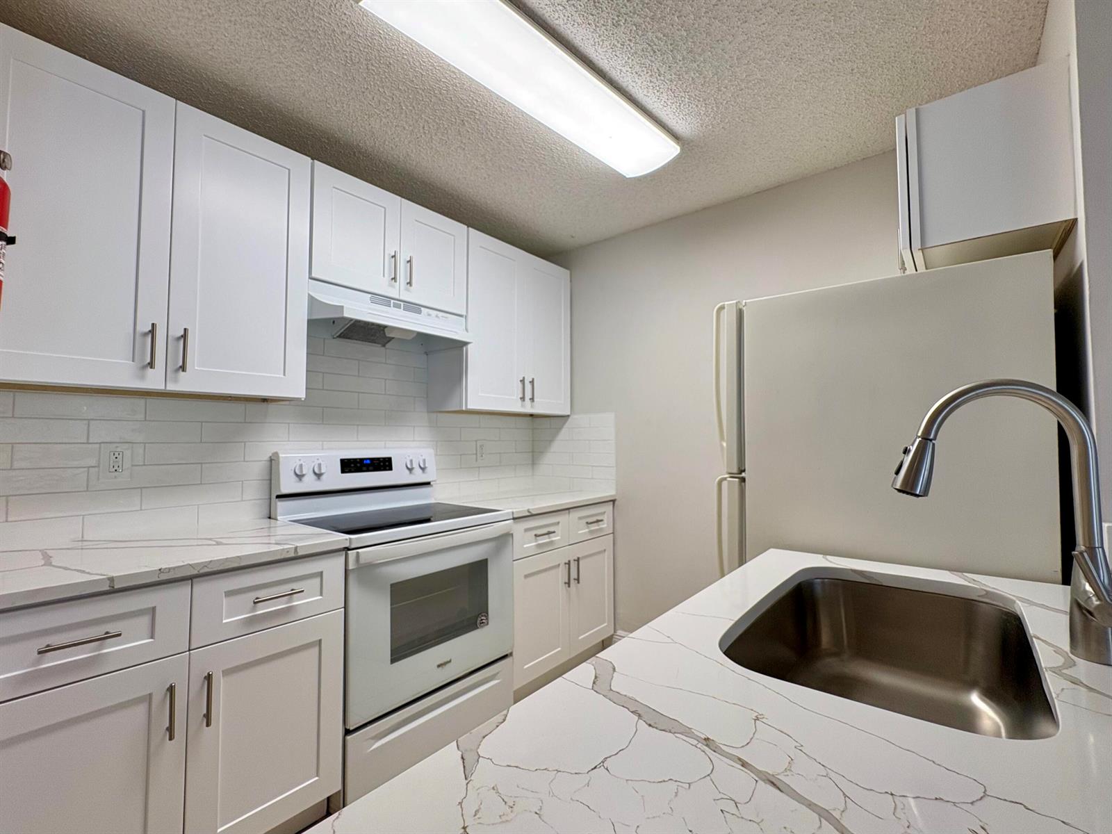 A kitchen features white cabinets, marble-patterned countertops, a stainless steel sink, and white appliances — 1830 W Meadows Circle # 1830, Boynton Beach FL 33436, BOYNTON BEACH, FL