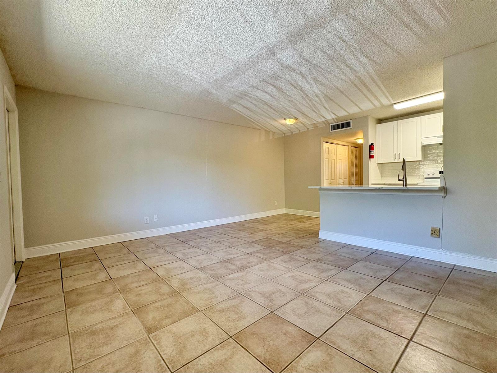 An open-concept living area features beige tile flooring, a popcorn ceiling, and a kitchen peninsula — 1830 W Meadows Circle # 1830, Boynton Beach FL 33436, BOYNTON BEACH, FL