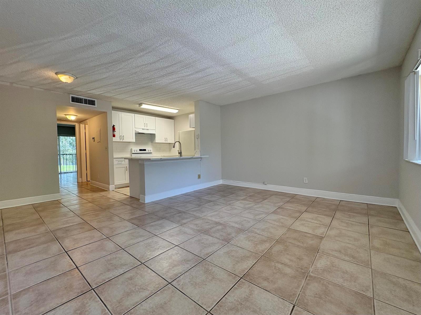 An open-concept living area features light-colored tile flooring, a kitchen with white cabinets, and a breakfast bar — 1830 W Meadows Circle # 1830, Boynton Beach FL 33436, BOYNTON BEACH, FL