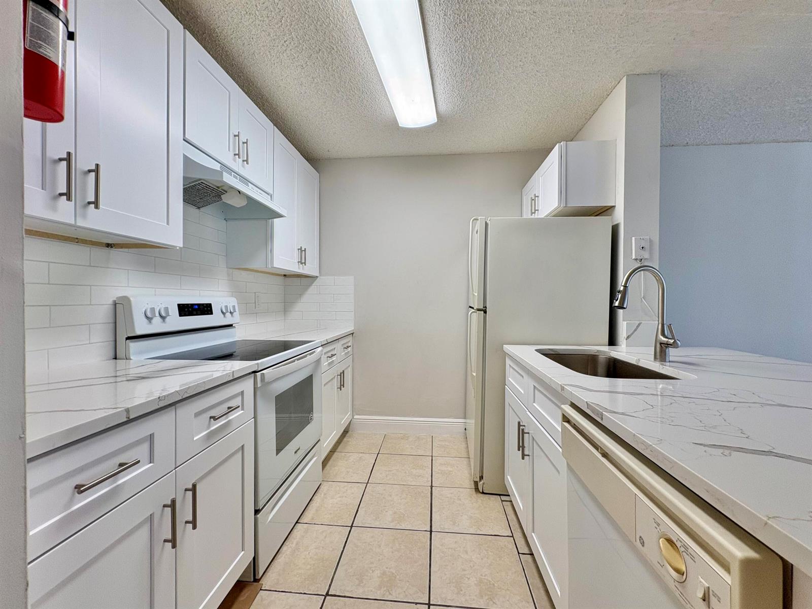 A galley kitchen features white cabinets, marble-look countertops, a white stove, and a refrigerator — 1830 W Meadows Circle # 1830, Boynton Beach FL 33436, BOYNTON BEACH, FL