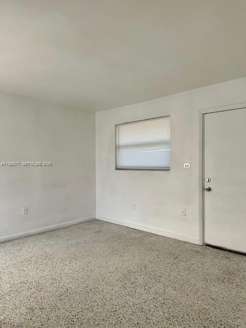 An empty room features white walls, a window with blinds, and speckled flooring — 129 NE 80th Ter # 6, Miami FL 33138, MIAMI, FL