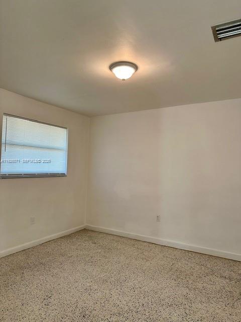 An empty room features white walls, a window with blinds, and speckled flooring — 129 NE 80th Ter # 6, Miami FL 33138, MIAMI, FL
