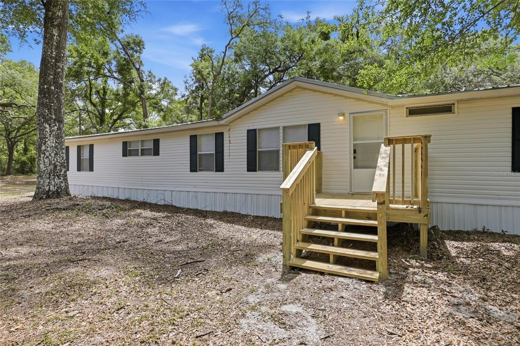 A single-story manufactured home with white siding and a new wooden deck entrance — 7651 NW 153RD LANE, CHIEFLAND, FL