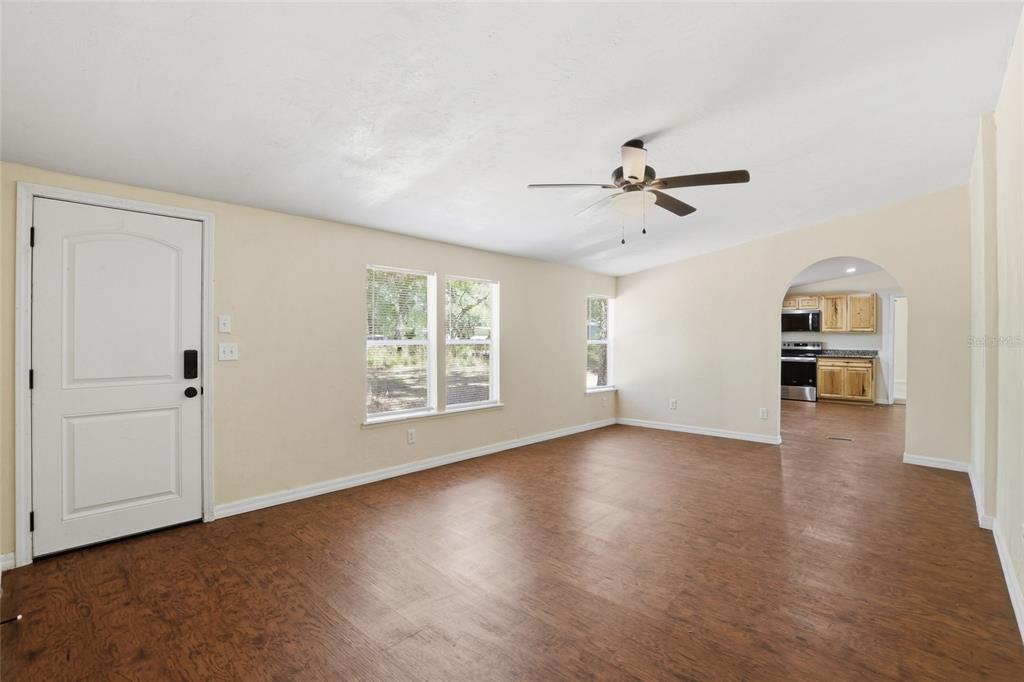 An empty living room features wood-look flooring, a ceiling fan, and an arched kitchen entryway — 7651 NW 153RD LANE, CHIEFLAND, FL