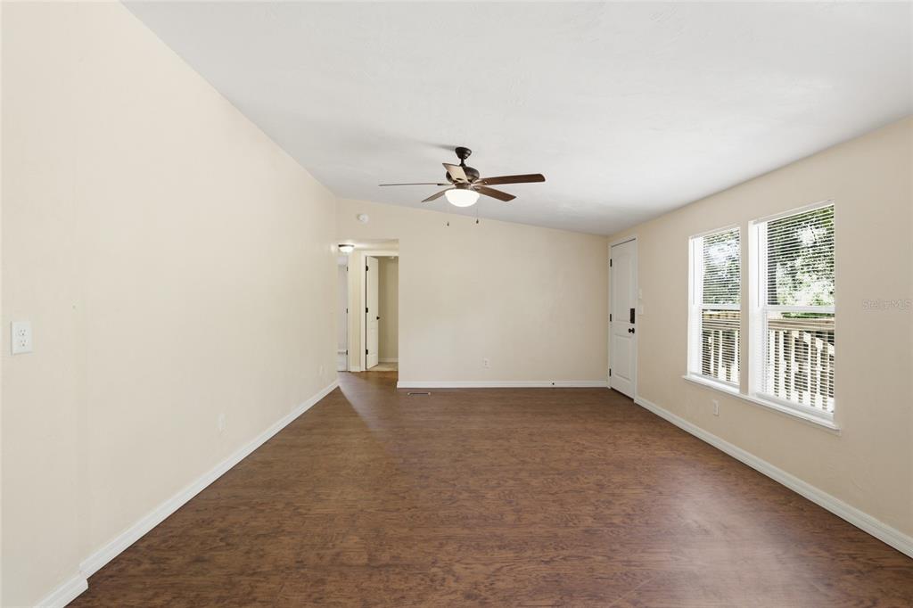 An empty living room features wood-look flooring, a ceiling fan, and two windows — 7651 NW 153RD LANE, CHIEFLAND, FL