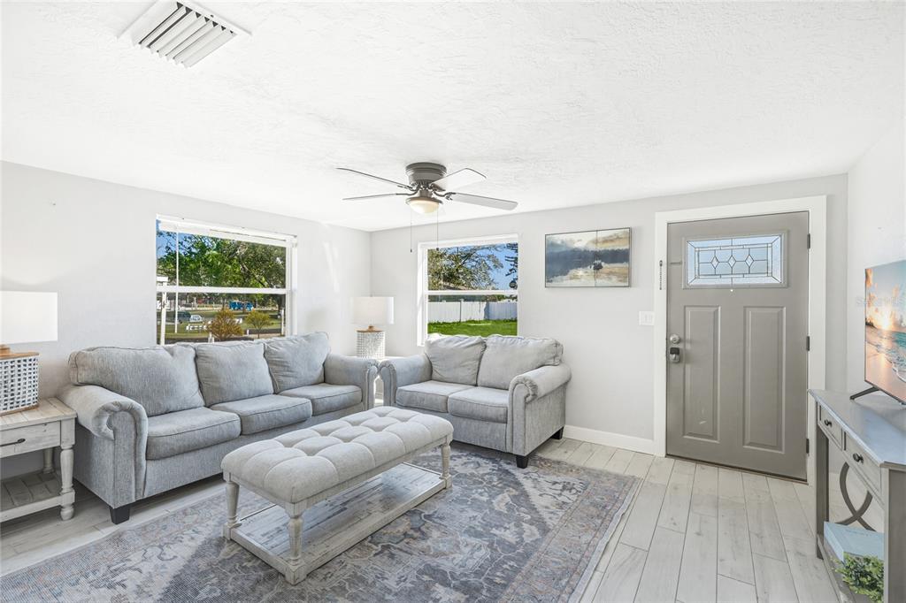 A living room features light gray walls, wood-look tile flooring, two sofas, and a front door — 5320 MOELLER AVENUE, SARASOTA, FL
