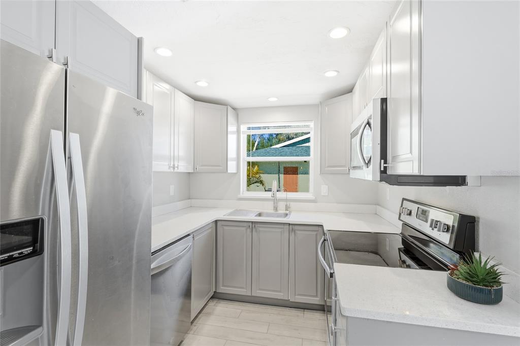 A kitchen features light gray cabinets, stainless steel appliances, white countertops, and a window — 5320 MOELLER AVENUE, SARASOTA, FL