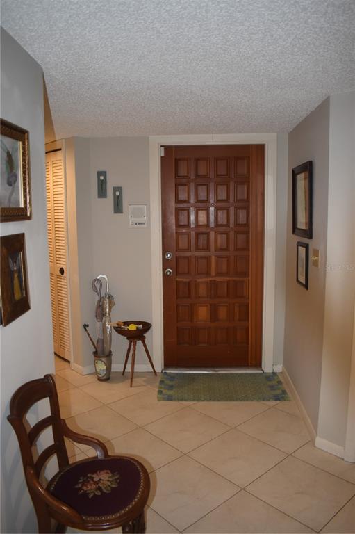 An entryway features a wooden door, tiled floor, a small chair, and wall art — 3053 EAGLES LANDING CIRCLE W UNIT 3053, CLEARWATER, FL