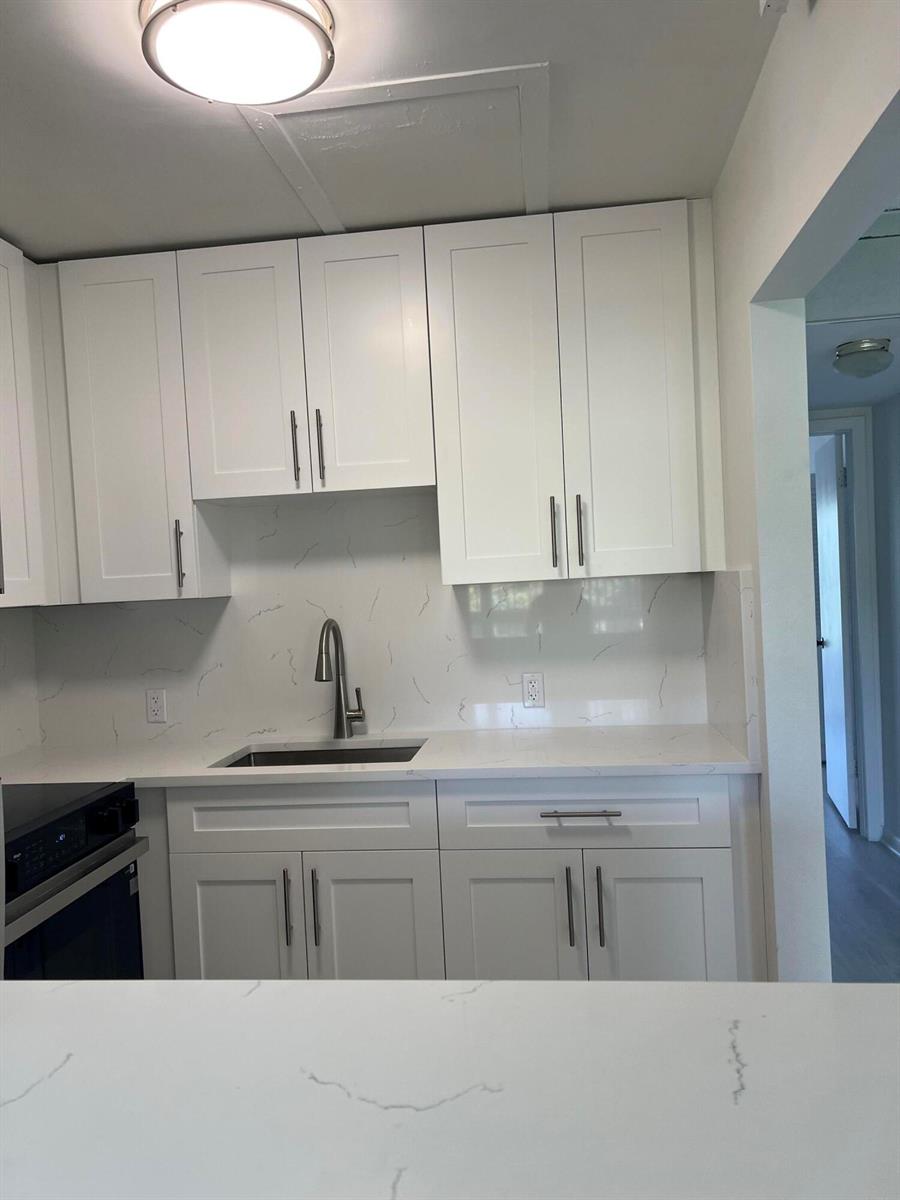A kitchen features white shaker cabinets, a marble-patterned backsplash, and a stainless steel sink — 36 Mansfield A, Boca Raton FL 33434, BOCA RATON, FL