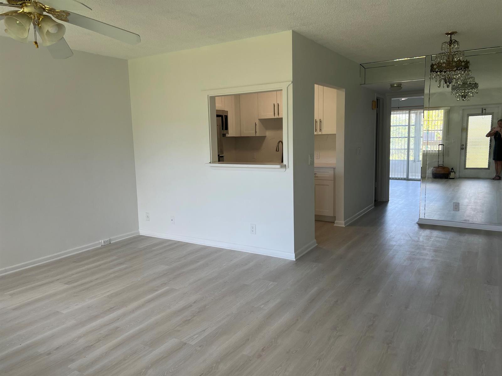 An open living area features light wood-look flooring, a kitchen pass-through, and mirrored walls — 36 Mansfield A, Boca Raton FL 33434, BOCA RATON, FL