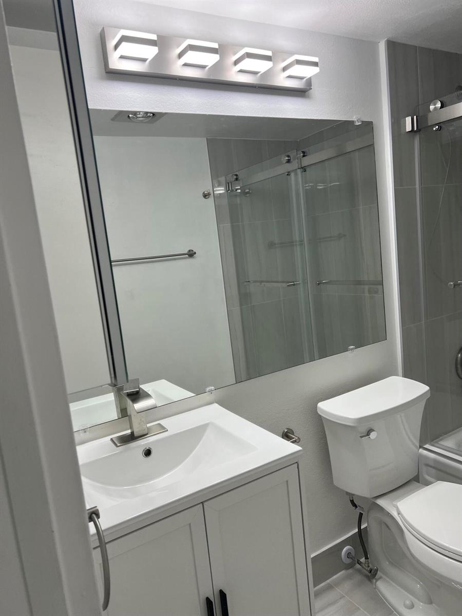 A bathroom features a white vanity, a large mirror, and a modern light fixture — 36 Mansfield A, Boca Raton FL 33434, BOCA RATON, FL