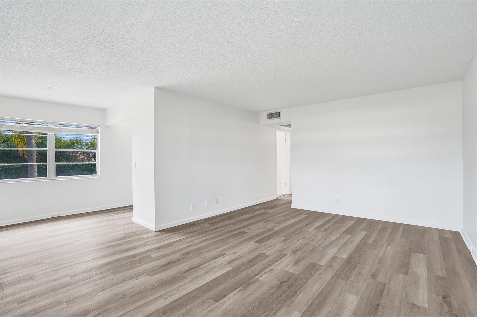 An empty room with white walls, wood-look flooring, and a window overlooking palm trees — 57 Dorset Drive # B, Boca Raton FL 33434, BOCA RATON, FL