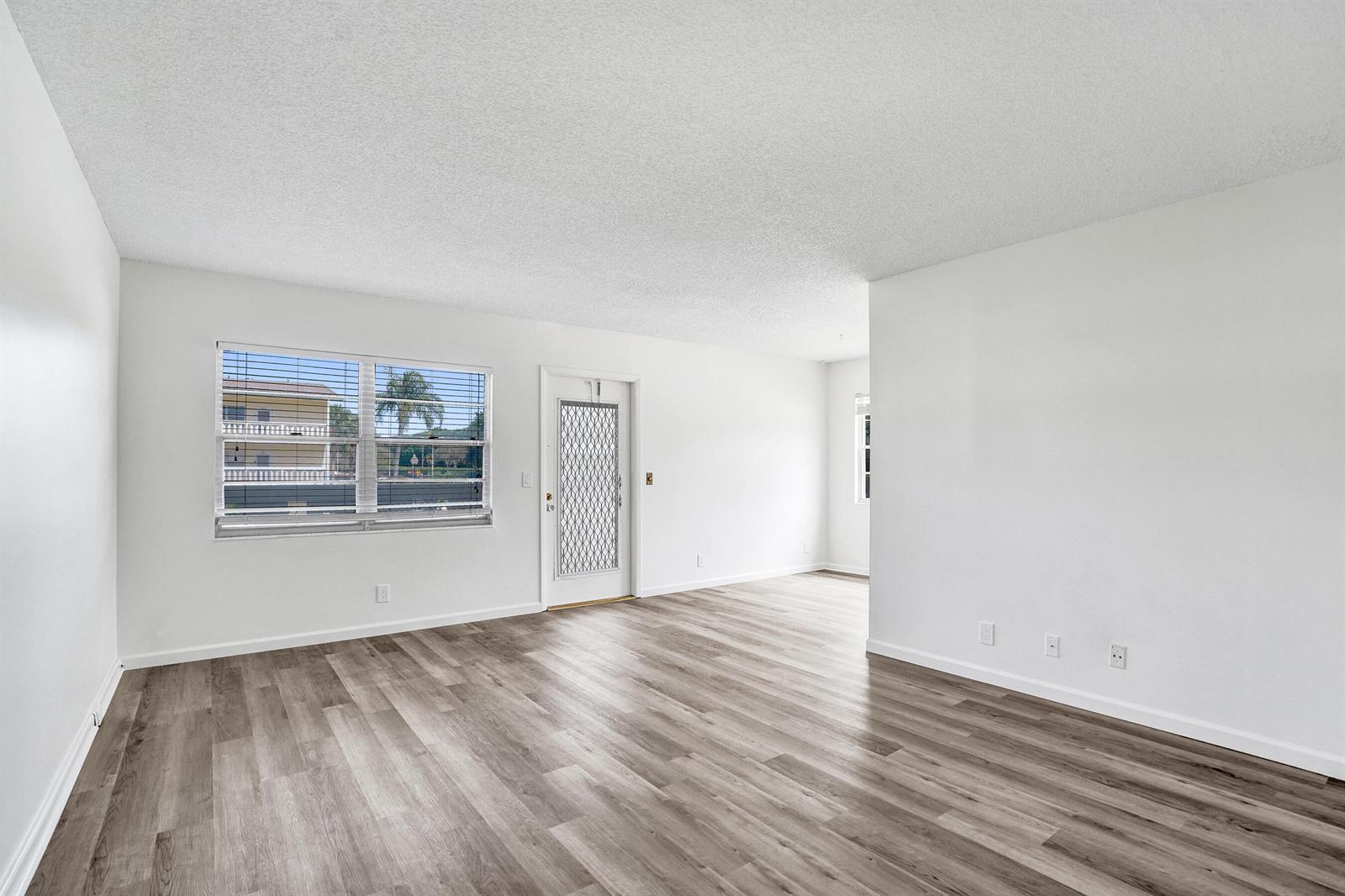 An empty living room features white walls, light wood-look flooring, and a front entry door — 57 Dorset Drive # B, Boca Raton FL 33434, BOCA RATON, FL