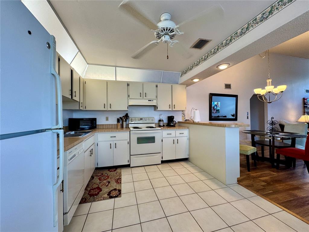 A kitchen with white cabinets, white appliances, and tiled floors opens to a dining area — 5400 34TH STREET W UNIT 12H, BRADENTON, FL