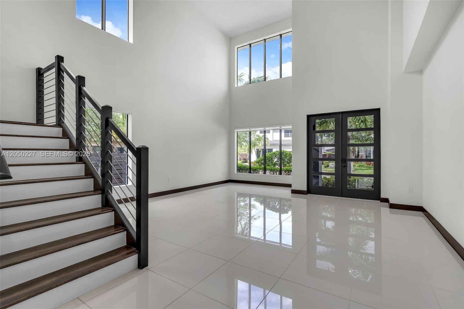 A bright, high-ceilinged foyer features white tile floors, a modern staircase, and large windows — 15455 NW 88th Ct, Miami Lakes FL 33018, MIAMI LAKES, FL
