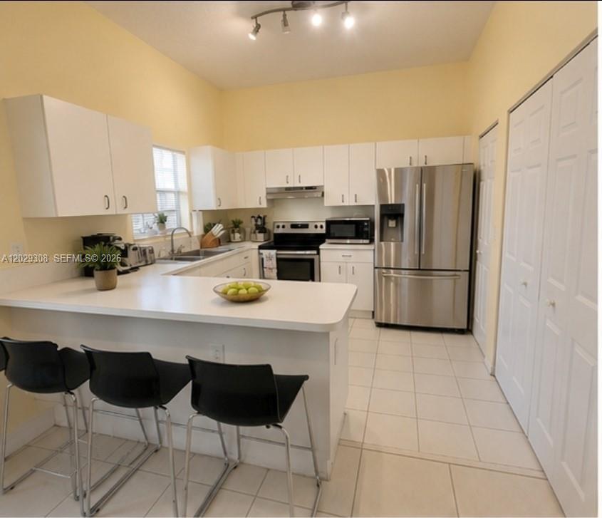A kitchen with white cabinets, stainless steel appliances, a breakfast bar, and tile flooring — 16143 Emerald Cove Rd, Weston FL 33331, WESTON, FL