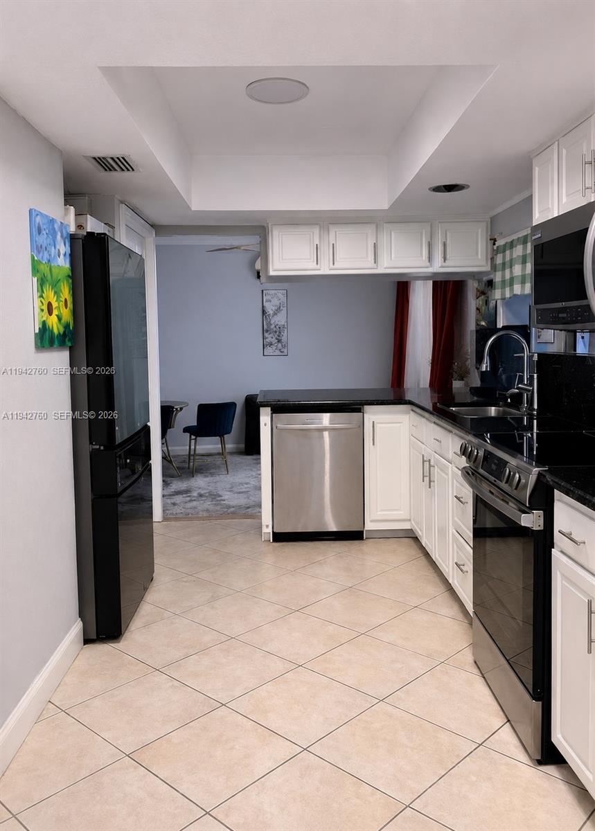 A kitchen features white cabinets, black countertops, stainless steel appliances, and beige tile flooring — 2450 NW 85th Ave, Sunrise FL 33322, SUNRISE, FL