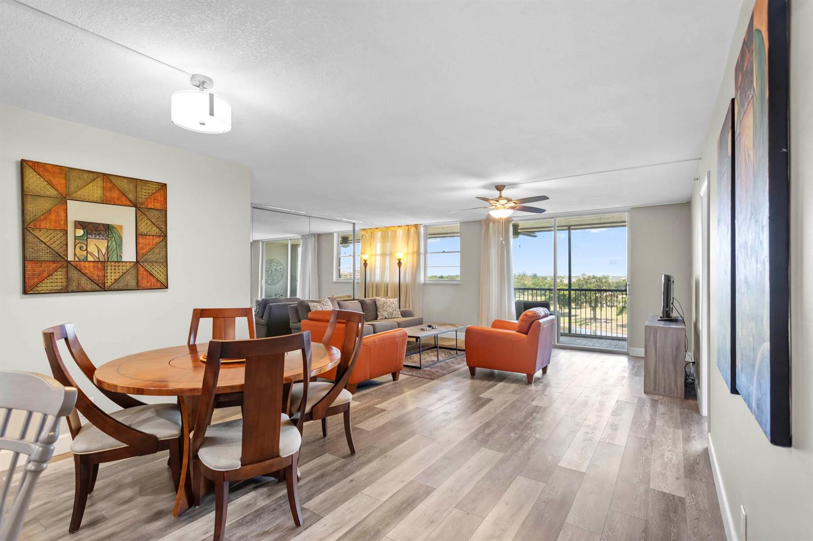 An open-concept living and dining area features wood-look flooring, orange armchairs, and a balcony view — 3150 W Rolling Hills Circle # 704, Davie FL 33328, DAVIE, FL