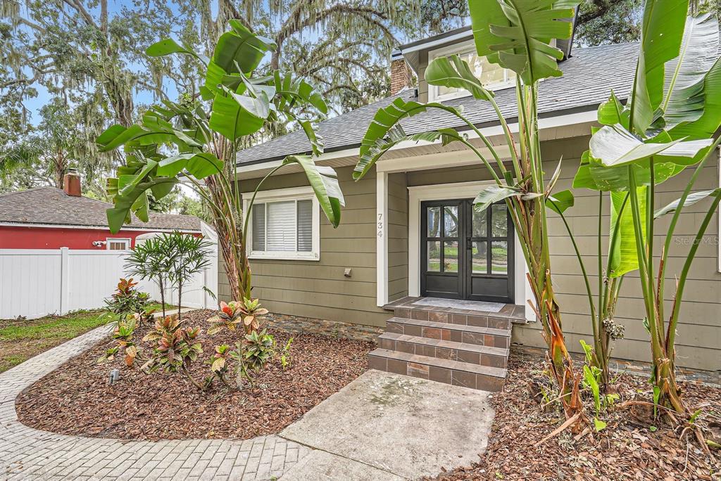 A house exterior features olive green siding, a tiled front entrance, and large tropical plants — 734 S MILLS AVENUE, ORLANDO, FL