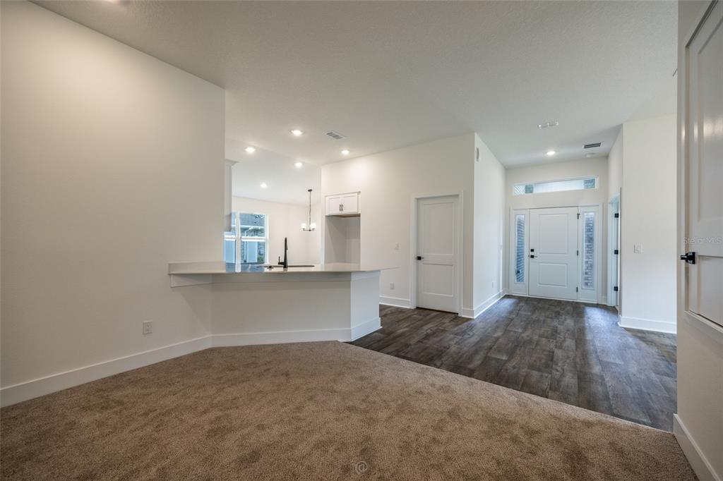 A living area with carpeted flooring transitions to a kitchen with a breakfast bar — 73 PRICE LANE, PALM COAST, FL