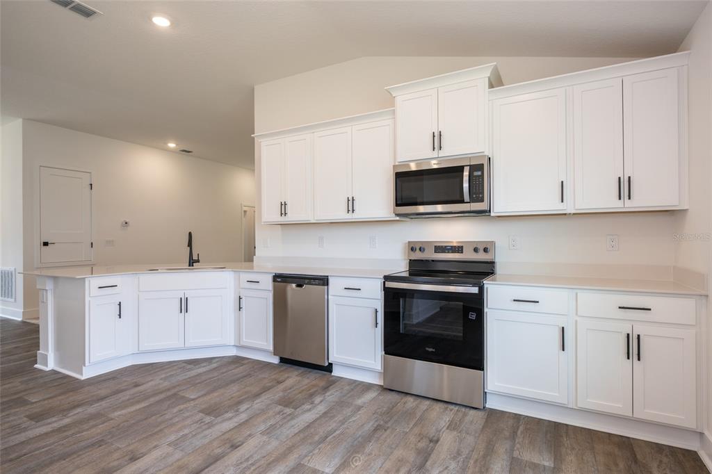 A kitchen features white cabinets, stainless steel appliances, and light-colored countertops over wood-look flooring — 73 PRICE LANE, PALM COAST, FL