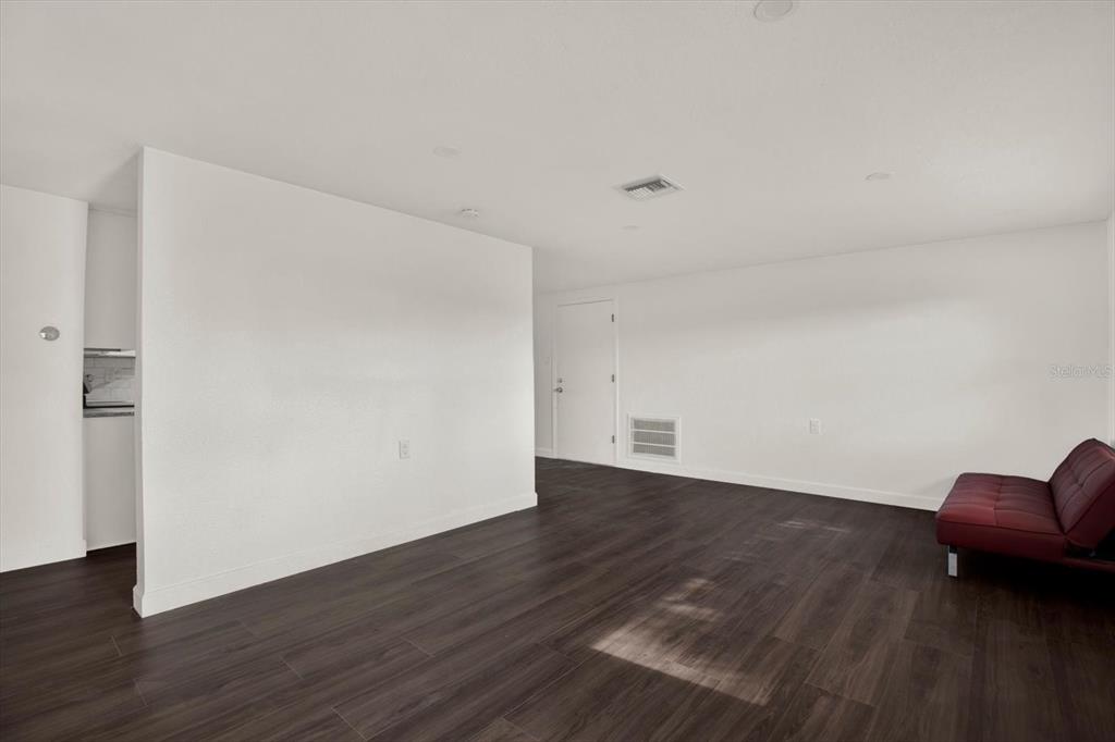 A living room with white walls, dark wood-look flooring, and a red futon — 13605 GARRIS DRIVE, HUDSON, FL