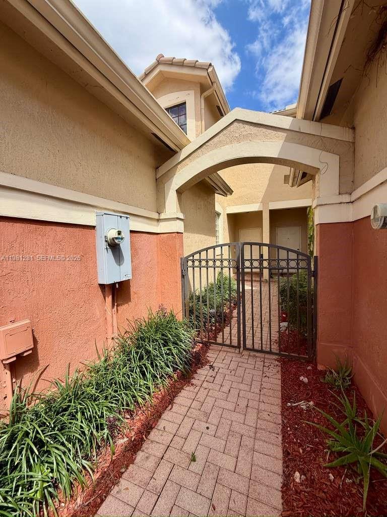 A brick walkway leads through a metal gate to the entrance of a stucco house — 3813 Tree Top Dr, Weston FL 33332, WESTON, FL