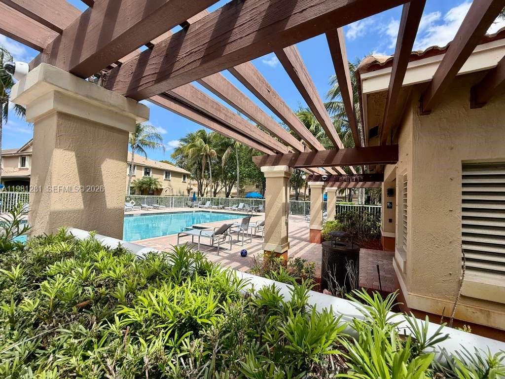 A wooden pergola covers a patio area overlooking a swimming pool and palm trees — 3813 Tree Top Dr, Weston FL 33332, WESTON, FL