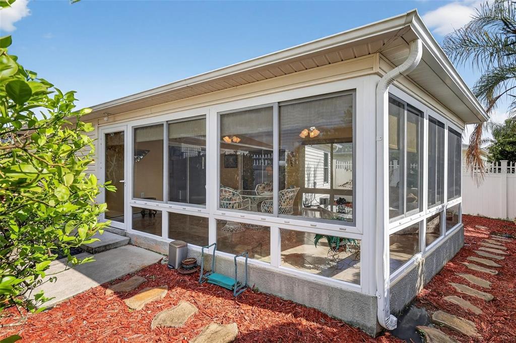 A sunroom with large windows and a white frame sits beside a red-mulched garden path — 1258 ESTILL AVENUE, THE VILLAGES, FL