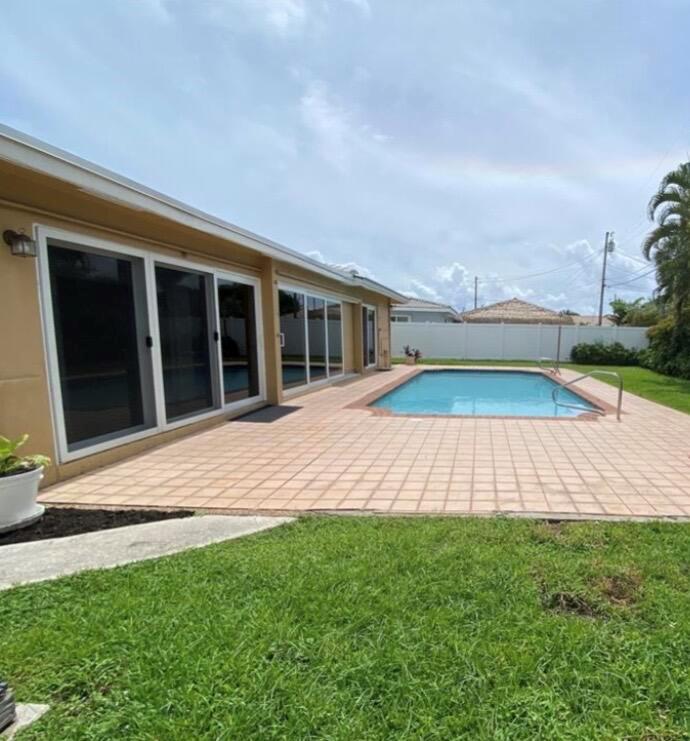 A backyard features a rectangular swimming pool, a tiled patio, and sliding glass doors — 1230 SE 14th Drive, Deerfield Beach FL 33441, DEERFIELD BEACH, FL