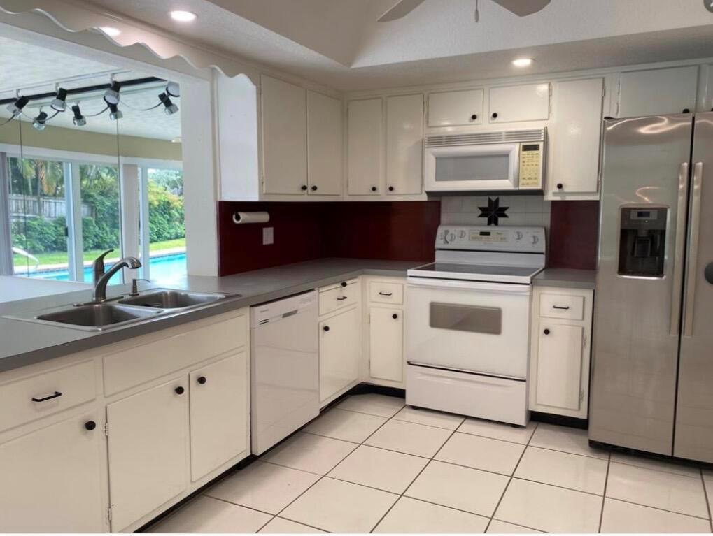 A kitchen features white cabinets, a dark red backsplash, stainless steel appliances, and tile flooring — 1230 SE 14th Drive, Deerfield Beach FL 33441, DEERFIELD BEACH, FL