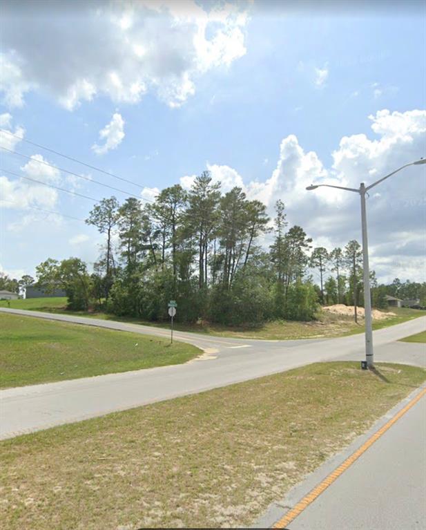 A paved intersection with a street sign and a tall light pole near wooded land — MARION OAKS TRAIL, OCALA, FL
