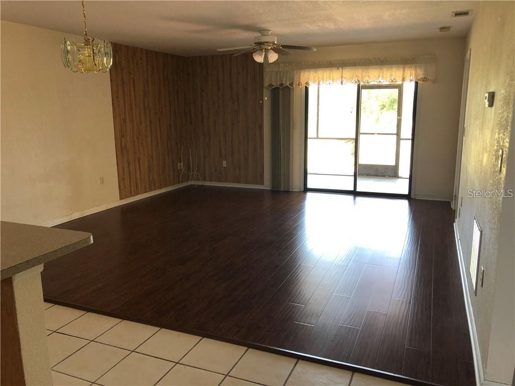 A living room features dark wood-look flooring, a wood-paneled wall, and a sliding glass door — 27082 ADAMS STREET UNIT B, PUNTA GORDA, FL