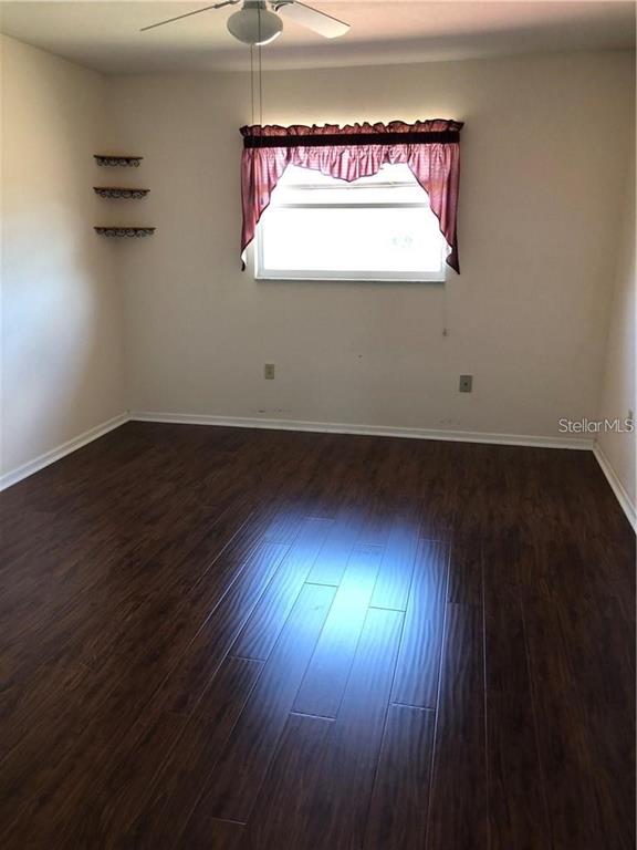 An empty room features dark wood-look flooring, a ceiling fan, and three small wall shelves — 27082 ADAMS STREET UNIT B, PUNTA GORDA, FL