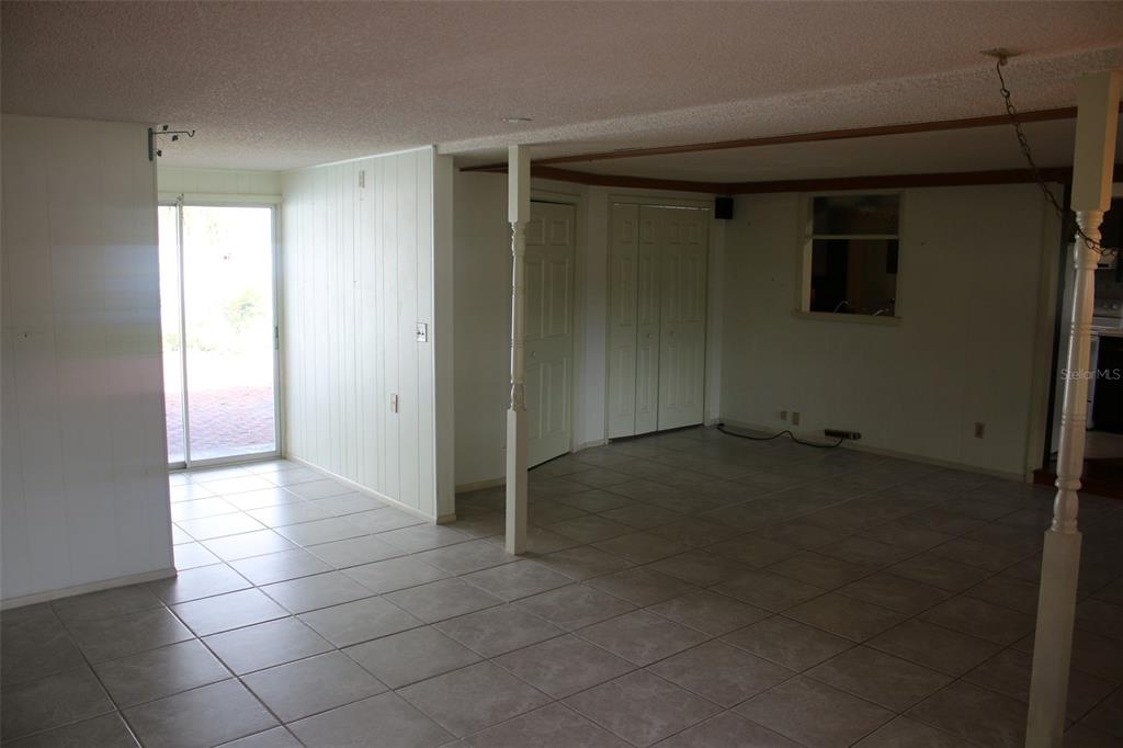 A room with light-colored tile flooring, wood-paneled walls, a sliding glass door, and support columns — 407 N POMPANO AVENUE, SARASOTA, FL