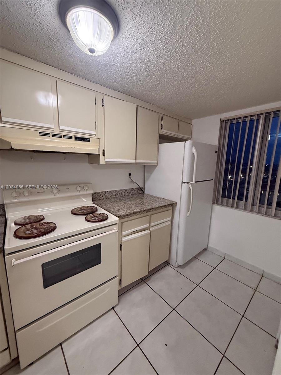 This kitchen features white appliances, beige cabinets, granite countertops, and white tile flooring — 9917 W Okeechobee Rd # 510, Hialeah Gardens FL 33016, HIALEAH GARDENS, FL