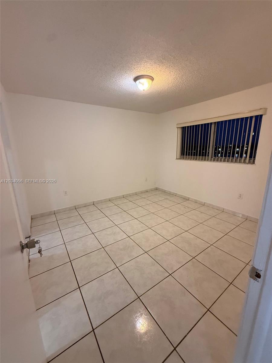 An empty bedroom features white walls, light-colored floor tiles, and a window with vertical blinds — 9917 W Okeechobee Rd # 510, Hialeah Gardens FL 33016, HIALEAH GARDENS, FL