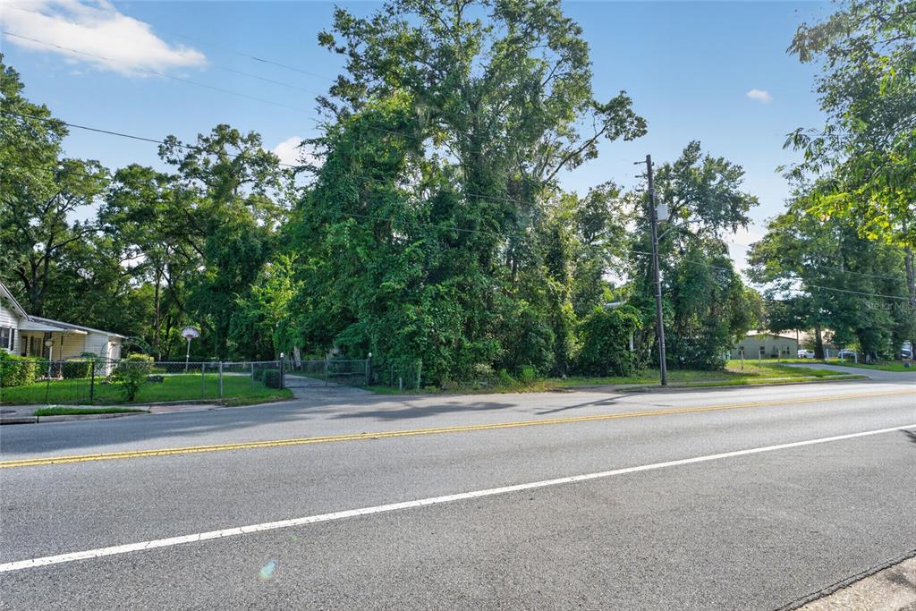 A paved road runs in front of a wooded lot with a gated entrance — TBD NW 1ST AVENUE, HIGH SPRINGS, FL