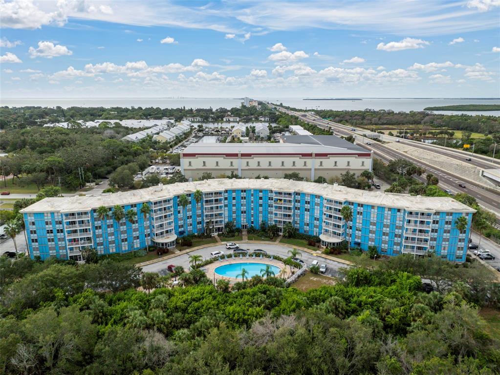 An aerial view shows a curved blue apartment building with a swimming pool in front — 3315 58TH AVENUE S UNIT 314, ST PETERSBURG, FL