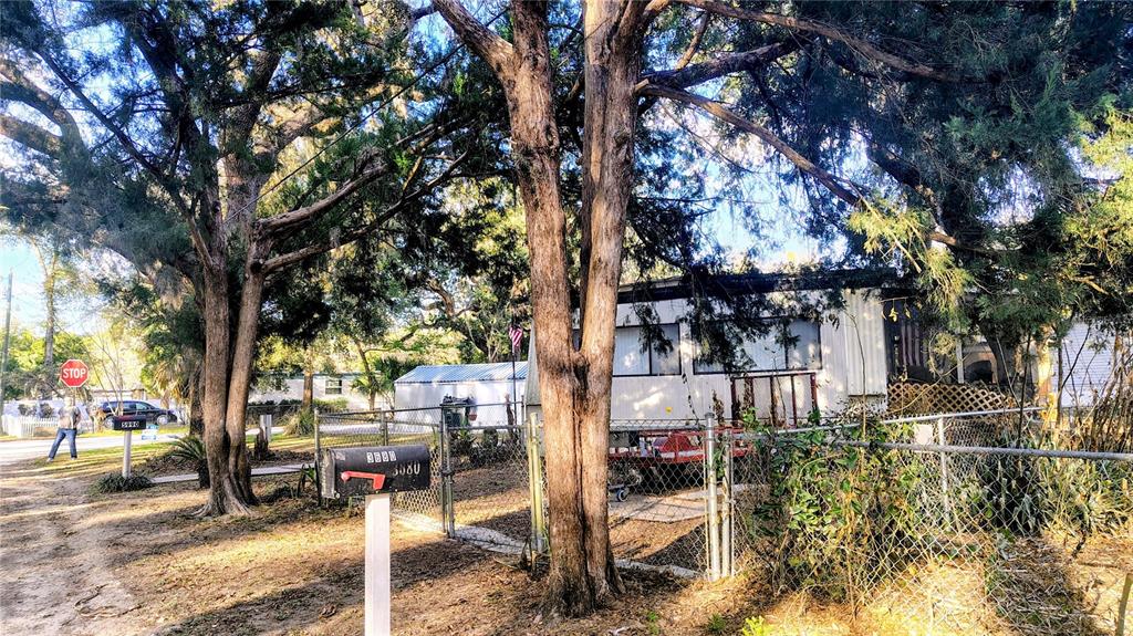 A mobile home sits behind a chain-link fence surrounded by large trees and a mailbox — 5990 NE 37TH STREET, SILVER SPRINGS, FL