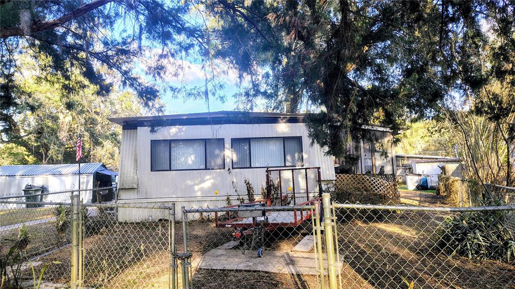 A single-story mobile home sits behind a chain-link fence with a trailer parked in front — 5990 NE 37TH STREET, SILVER SPRINGS, FL