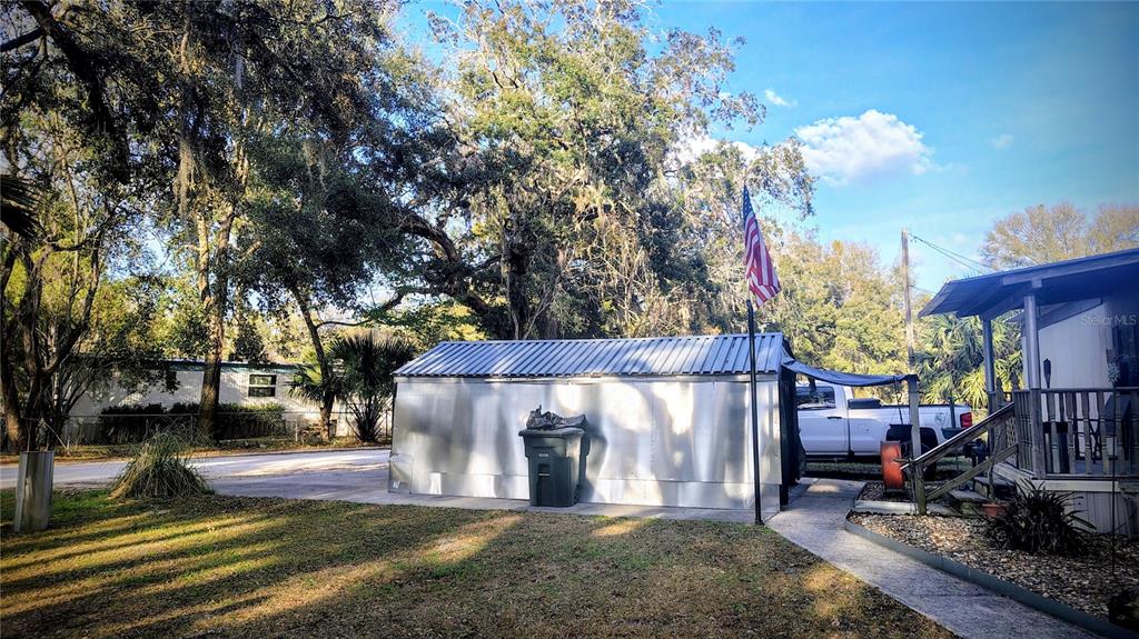 A metal shed stands on a concrete pad next to a house and driveway — 5990 NE 37TH STREET, SILVER SPRINGS, FL