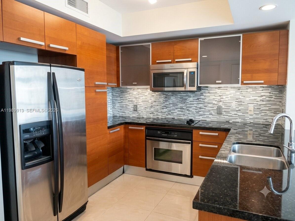 A kitchen features wood cabinets, stainless steel appliances, a mosaic backsplash, and dark granite countertops — 2030 S Douglas Rd # 414, Coral Gables FL 33134, CORAL GABLES, FL