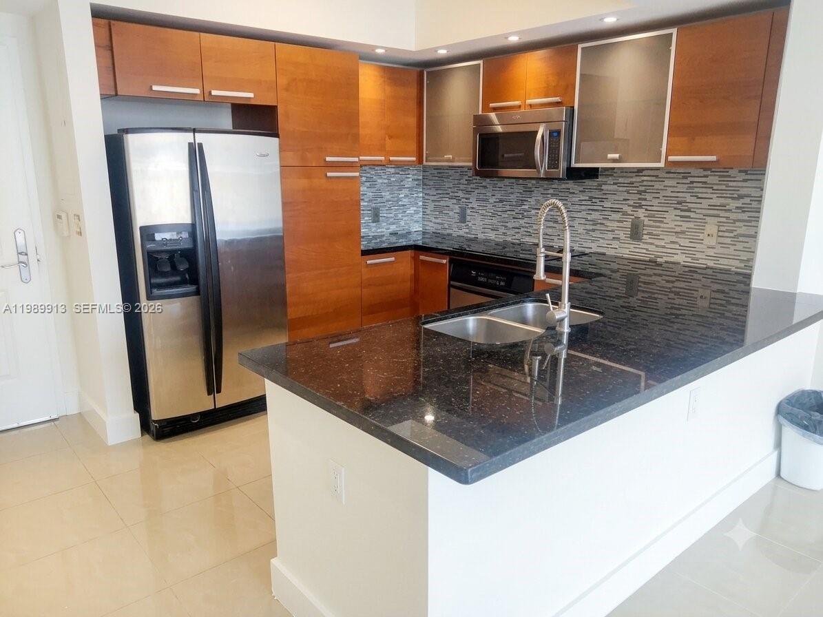 A kitchen features wood cabinets, stainless steel appliances, and a dark granite countertop island — 2030 S Douglas Rd # 414, Coral Gables FL 33134, CORAL GABLES, FL