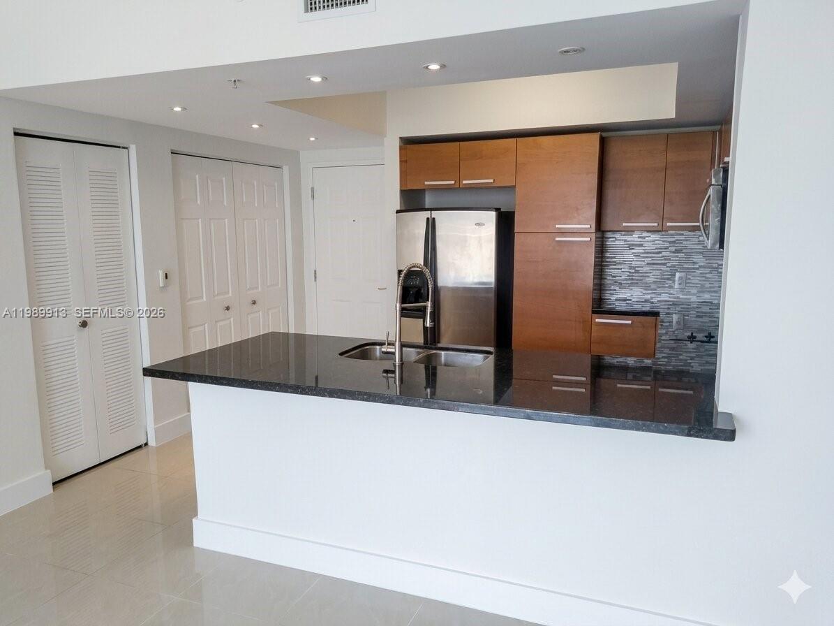 A kitchen features a black granite island, stainless steel appliances, and wood-toned cabinetry — 2030 S Douglas Rd # 414, Coral Gables FL 33134, CORAL GABLES, FL