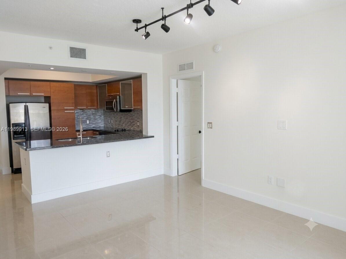 An open-concept kitchen with wood cabinets and a breakfast bar overlooks a tiled living area — 2030 S Douglas Rd # 414, Coral Gables FL 33134, CORAL GABLES, FL