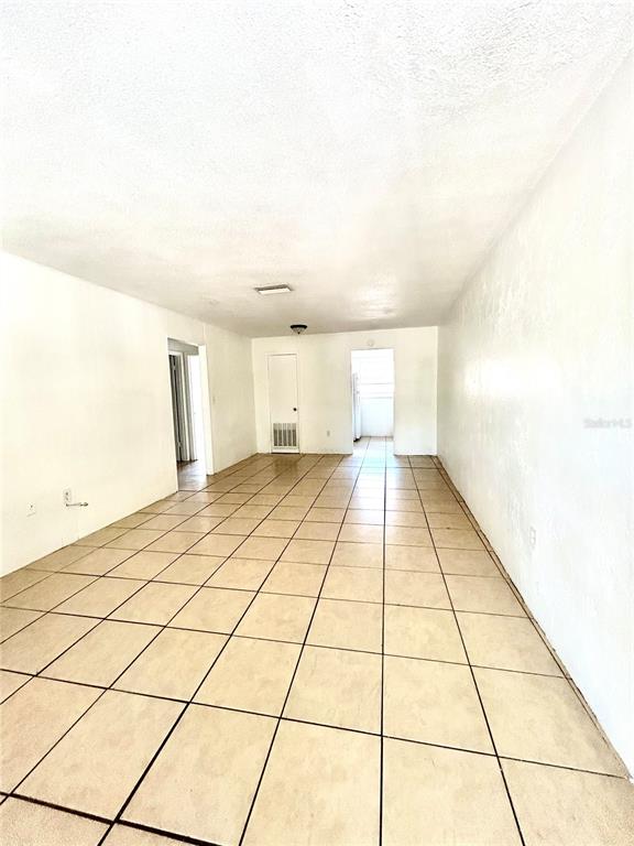 An empty room with white walls and beige tiled flooring leads to a doorway — 1217 KENNEDY ROAD UNIT 06, DAYTONA BEACH, FL