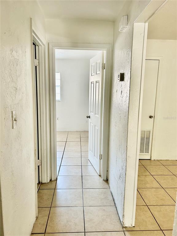 A hallway with beige tile flooring leads to an open doorway revealing a bedroom — 1217 KENNEDY ROAD UNIT 06, DAYTONA BEACH, FL