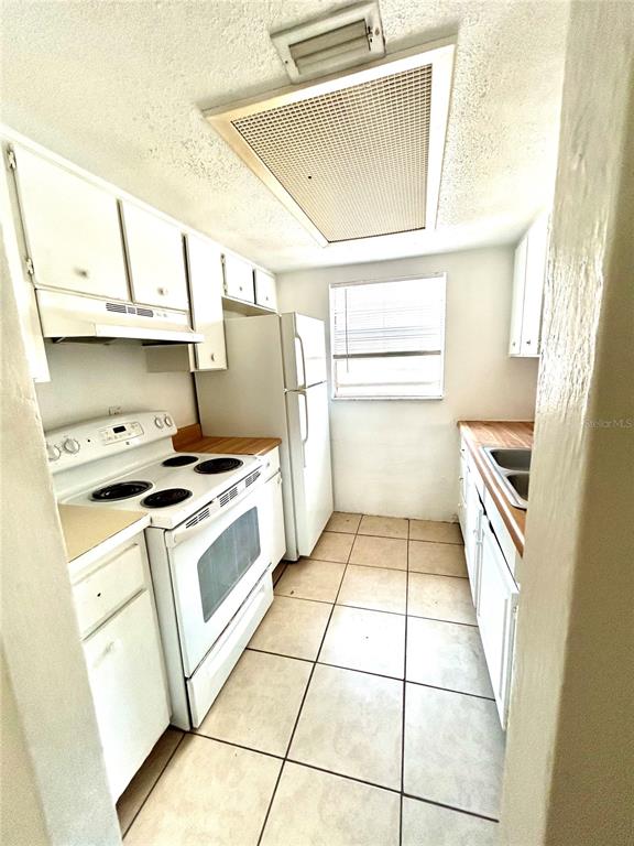 A galley kitchen features white cabinets, a white stove, a refrigerator, and tiled flooring — 1217 KENNEDY ROAD UNIT 06, DAYTONA BEACH, FL
