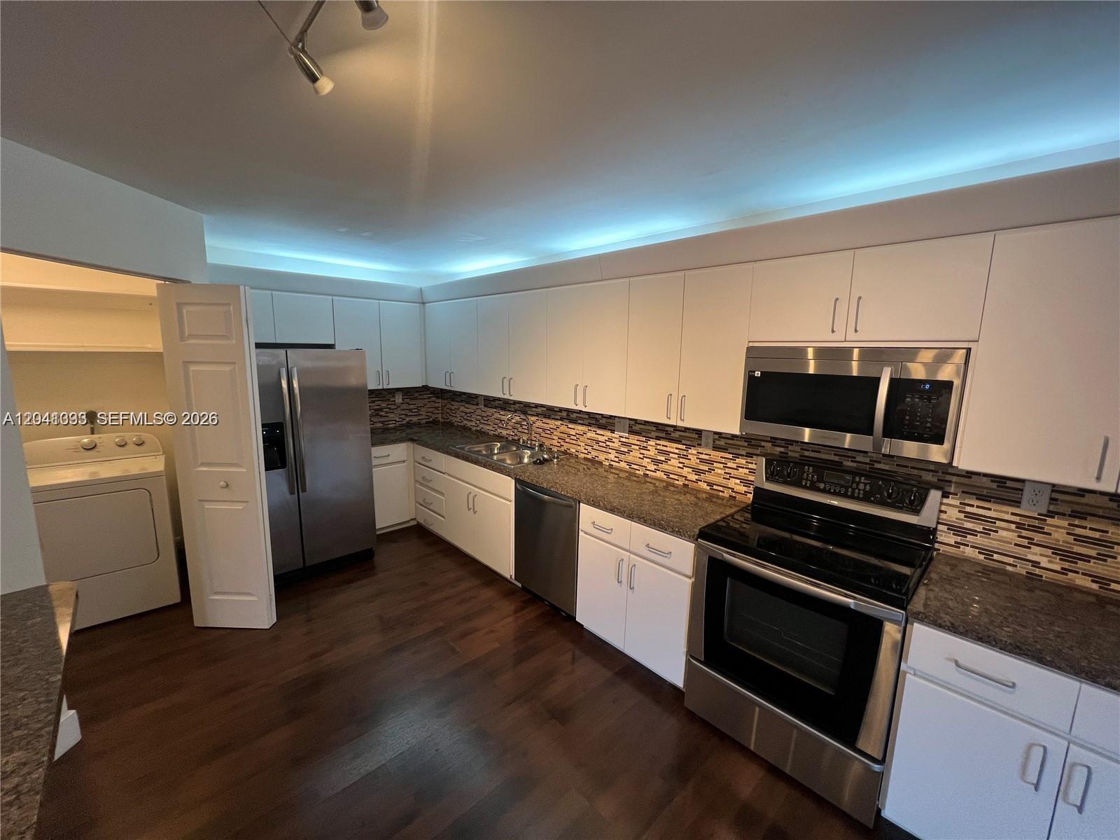 A kitchen features white cabinets, stainless steel appliances, granite countertops, and dark wood flooring — 561 Racquet Club Rd # 21, Weston FL 33326, WESTON, FL